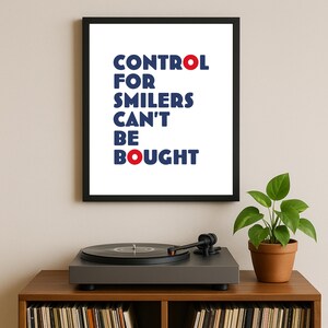 Può includere: Una stampa incorniciata con il testo "CONTROL FOR SMILERS CAN'T BE BOUGHT" in blu e rosso. La stampa è esposta sopra un giradischi su un mobile in legno con dischi in vinile. Una pianta in vaso è a destra.