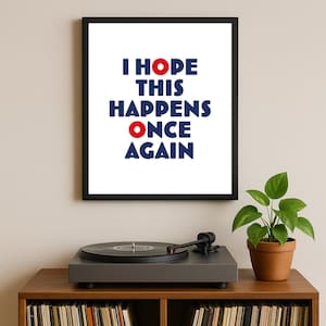Puede incluir: Impresión artística enmarcada con el texto "I HOPE THIS HAPPENS ONCE AGAIN" en azul y rojo. La impresión se muestra en un mueble de madera con un tocadiscos y una planta en maceta.