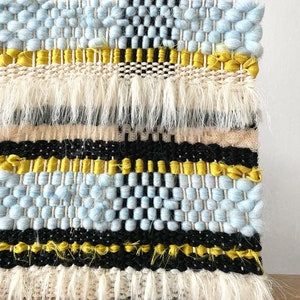 May include: A woven wall hanging with a blue, black, and yellow geometric pattern. The hanging has a fringe border.