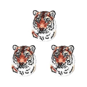May include: Three embroidered patches, each featuring the head of a tiger. The tiger faces are rendered in shades of orange, white, and black thread, showcasing detailed facial features, pointed ears, and distinct black stripes on a white background.