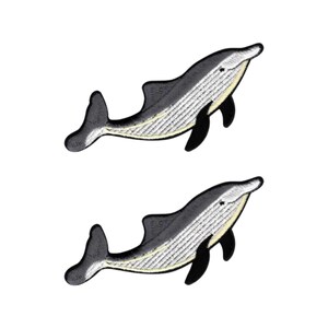 May include: Two identical embroidered patches, each depicting a whale in profile. The whales feature a dark gray upper body, a white underbelly with vertical textured lines, a black dorsal fin, and a black pectoral fin, all outlined in black.