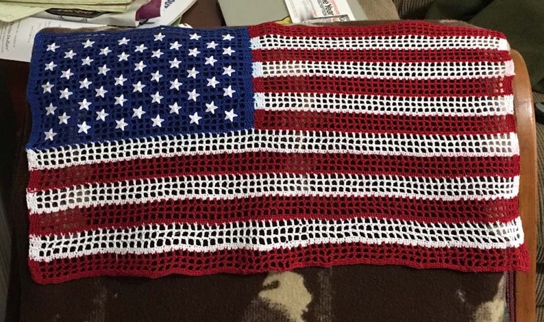 Op de afbeelding: Een gehaakt Amerikaans vlaggenkleed in rood, wit en blauw. De vlag is gemaakt met een gaaspatroon en heeft een gefranst randje.