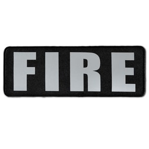 May include: A rectangular black patch with rounded corners featuring the word FIRE in large, bold, reflective silver capital letters. The text is centered on the fabric surface, which has a visible woven texture and a stitched border edge.