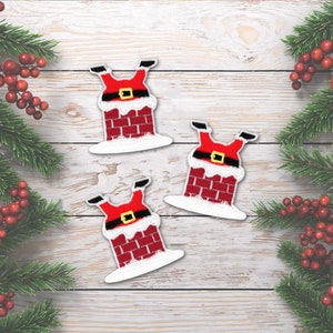 May include: Three embroidered patches featuring Santa Claus legs sticking out of a red brick chimney. The design includes a black belt with a yellow buckle, white snow trim on the chimney top, and white snow at the base of the brick structure.