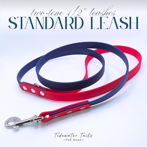 May include: A two-tone 1/2 inch standard leash featuring a navy blue and red strap with silver-colored metal rivets and a swivel snap hook. The text two-tone 1/2 inch leashes, STANDARD LEASH, and Tidewater Tails - Pet Gear - are visible.