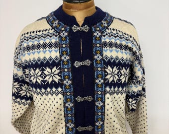 Könnte beinhalten: Cremefarbene Wollstrickjacke mit marineblauem Kragen und Besatz. Der Pullover hat ein Schneeflocken- und geometrisches Muster in Marineblau und Hellblau. Er hat silberfarbene Verschlüsse vorne. Auf einer Schaufensterpuppe.
