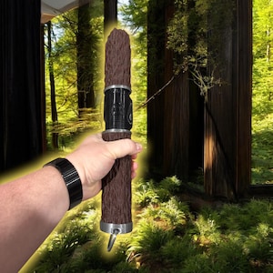 Peut inclure: Un sabre laser en bois brun avec une poignée en métal noir et une bague argentée. Le sabre laser a une surface texturée et une boucle en bas.
