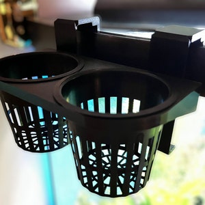 May include: Black plastic aquarium plant holder with two round baskets. The baskets have a lattice design and are attached to a bracket that can be mounted on the edge of an aquarium. The holder is designed to hold aquatic plants.