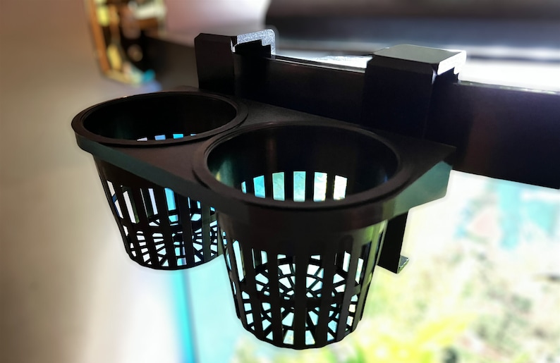 May include: Black plastic aquarium plant holder with two round baskets. The baskets have a lattice design and are attached to a bracket that can be mounted on the edge of an aquarium. The holder is designed to hold aquatic plants.