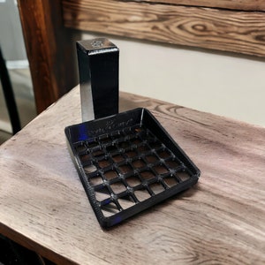 Puede incluir: Un jabonera de plástico negro con un patrón de rejilla y un dispensador de jabón de plástico negro con una parte superior cromada. La jabonera y el dispensador están sobre una superficie de madera.