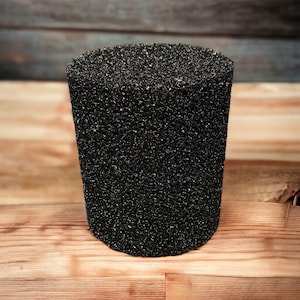 Puede incluir: Un filtro de esponja negro cilíndrico con una superficie texturizada. El filtro está hecho de un material poroso y está diseñado para su uso en acuarios.