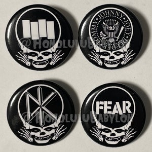 以下が含まれることがあります： 骸骨と交差した骨のデザインが施された、黒と白のボタンピンが4つ。各ピンには、Black Flag、Fear、The Misfits、The Dead Kennedysという異なるバンドのロゴが描かれています。
