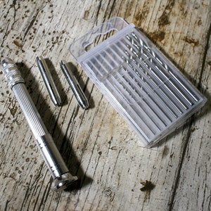 May include: A set of drill bits for jewelry making, including a hand drill with a silver finish and a clear plastic case containing multiple drill bits.
