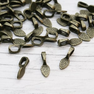 Könnte beinhalten: Eine große Menge antiker goldfarbener Metall-Anhängerösen. Die Ösen sind tropfenförmig mit einer kleinen Öse oben. Die Ösen haben eine strukturierte Oberfläche.