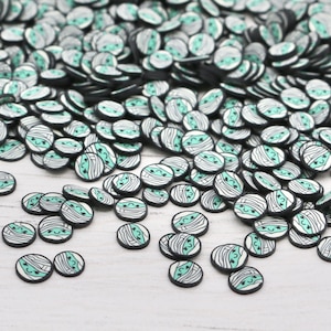 May include: A large pile of small, round, white and black resin flatback cabochons with a green and white mummy design.