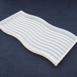 May include: White plastic tray with a wavy design and parallel ridges. The tray is designed to hold multiple items.
