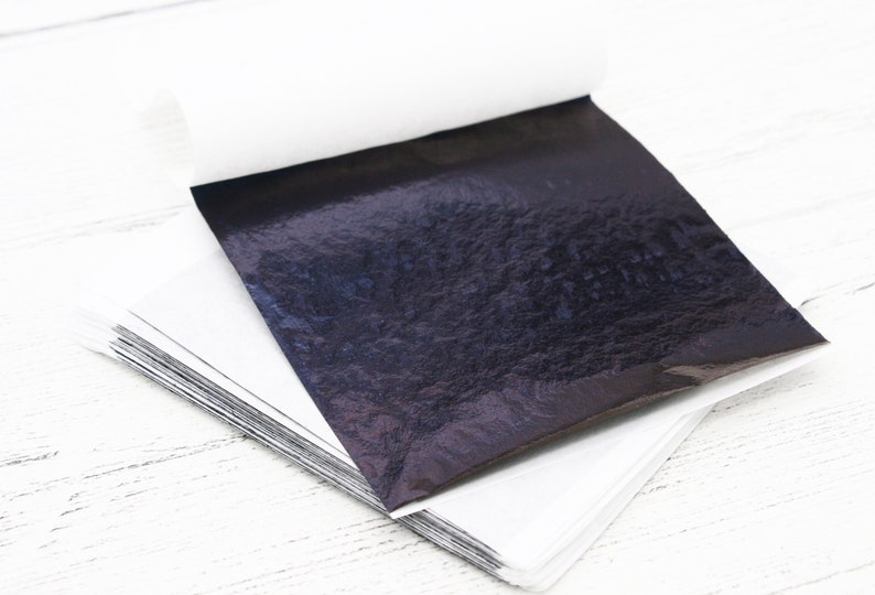 May include: A stack of black metallic leaf sheets, with a single sheet unfolded and lying on top. The sheets have a textured, iridescent finish.