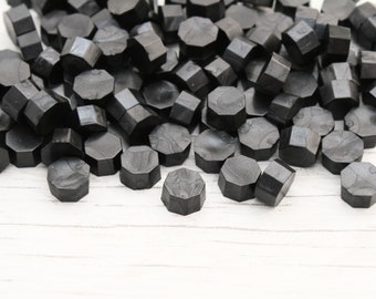 May include: A pile of black wax seals, scattered on a white wooden surface. The seals are hexagonal in shape and have a slightly textured surface.