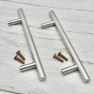 May include: Two silver cabinet pulls with a T-shaped handle and screws.