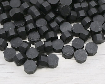 May include: A large quantity of black wax seals, each with a hexagonal shape. The seals are scattered on a white surface.