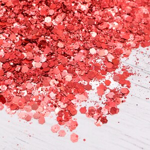 May include: A close-up of a pile of red glitter on a white surface. The glitter is made up of small, hexagonal pieces.