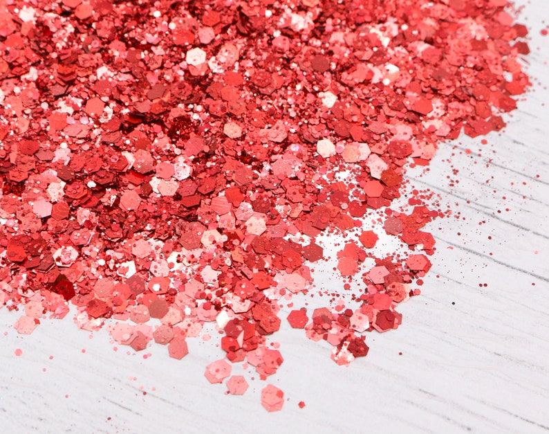 May include: A close-up of a pile of red glitter on a white surface. The glitter is made up of small, hexagonal pieces.