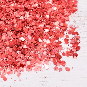 May include: A close-up of a pile of loose, sparkly, coral-colored glitter on a white surface.