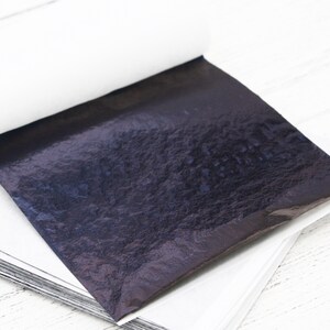 May include: A stack of thin, black, metallic sheets, with a single sheet partially unfolded, revealing a textured, iridescent surface.