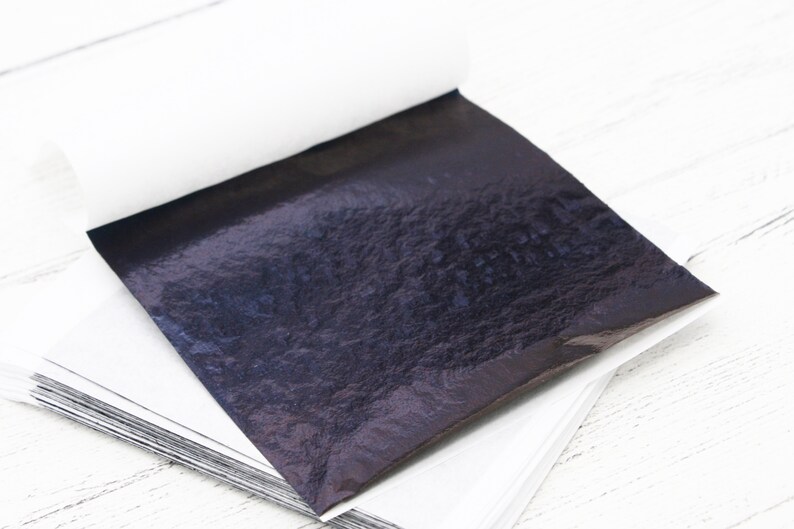May include: A stack of thin, black, metallic sheets, with a single sheet partially unfolded, revealing a textured, iridescent surface.