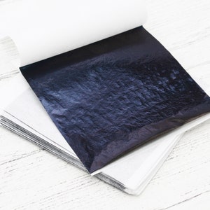 May include: A stack of thin, black, metallic sheets of transfer leaf, with a slightly textured surface, on a white background.