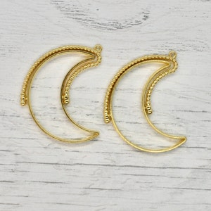 May include: Two gold metal crescent moon shaped frames. The frames are made of a beaded wire.
