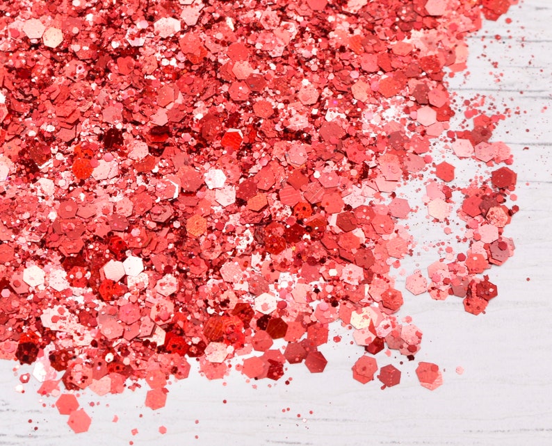 May include: A close-up of a pile of red glitter, scattered on a white surface.