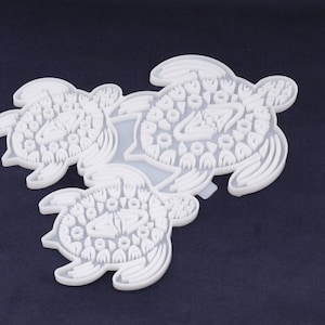 May include: Three white silicone molds shaped like sea turtles. Each turtle is decorated with a pattern of small circles and ovals.