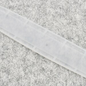May include: A white plastic tile spacer with a rectangular shape and a smooth surface.