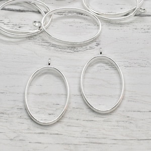 Puede incluir: Un conjunto de marcos de metal ovalados de color plateado con un bucle en la parte superior. Los marcos son perfectos para crear joyas o manualidades personalizadas.
