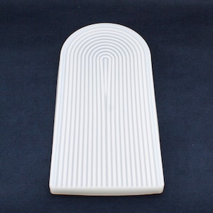 May include: White ceramic arch-shaped tray with a series of raised lines forming a pattern.