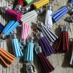 May include: Assortment of colorful suede tassels with silver metal tops. The tassels are various shades of blue, pink, red, orange, green, and gray.
