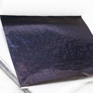 May include: A stack of thin, black, metallic sheets of transfer leaf. The sheets are on a white surface.