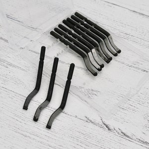 May include: A clear plastic case containing a set of black metal tools. The tools are shaped like a curved hook and are arranged in rows within the case.