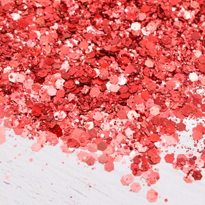 May include: A close-up of a pile of red glitter. The glitter is scattered on a white surface.