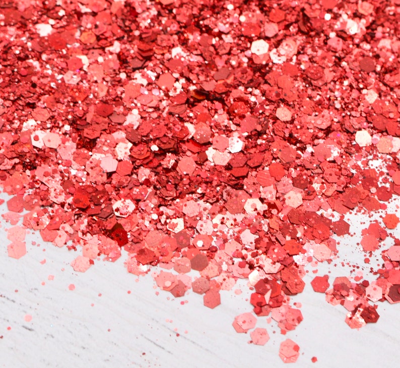 May include: A close-up of a pile of red glitter. The glitter is scattered on a white surface.