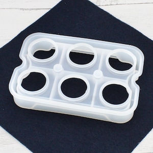 May include: A clear plastic mould with six round cavities, designed for making resin crafts.