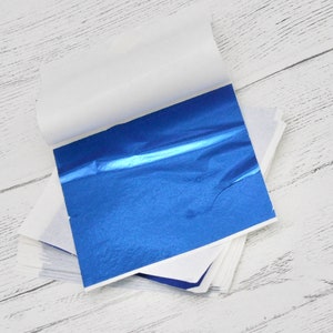 May include: A stack of blue metallic leaf sheets, with a single sheet partially unfolded, revealing the shiny blue surface.