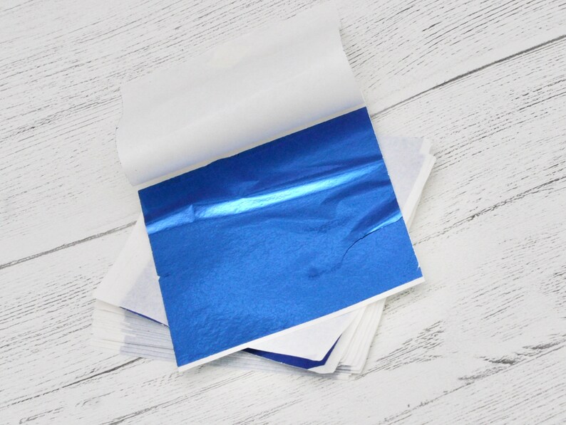 May include: A stack of blue metallic leaf sheets, with a single sheet partially unfolded, revealing the shiny blue surface.