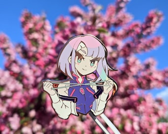 May include: A metal enamel pin featuring an anime-style character with short pink and light purple hair, wearing a dark blue and white jacket, holding a pair of chopsticks horizontally in front of their chest against a clear blue sky background.