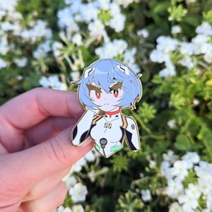 Op de afbeelding: Een gouden emaille pin met een cartoon anime-personage met blauw haar, rode ogen en een wit en zwart outfit. Het personage draagt een witte kraag met de letter "N" erop.
