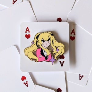 May include: A gold-colored enamel pin featuring a cartoon character with blonde hair, wearing a pink blazer and a white shirt. The character has a serious expression and is holding their hands together. The pin is set against a white background with red hearts and the letter 'A' in red.