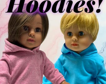May include: Two dolls with realistic features wearing long-sleeved hooded sweatshirts. One doll has brown hair and a pink hoodie, while the other has blonde hair and a bright blue hoodie. The text "Hoodies!" is displayed in large black letters above them.