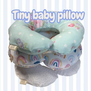 May include: Stack of handmade baby pillows in various patterns. The top pillow is light blue with white polka dots and floral accents. Other pillows feature rainbow and floral designs. The text "Tiny baby pillow" is above the pillows.