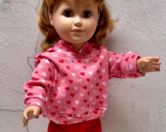 May include: A pink hooded sweatshirt with a white heart pattern for a doll. The sweatshirt has long sleeves and a drawstring hood.